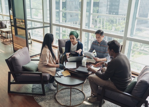 Four co-workers gather around a coffee table and discuss a project.