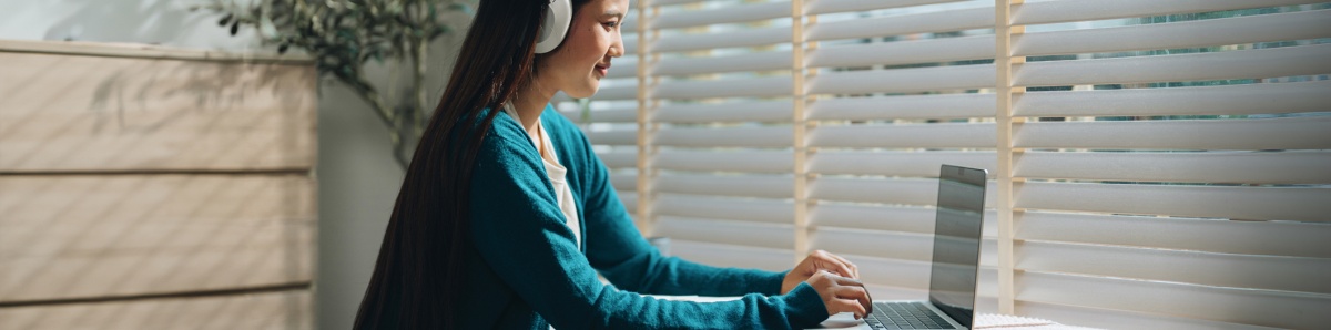 Woman sitting at a desk, typing on laptop with headphones in an indoor setting.