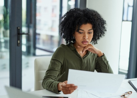 Woman reviewing paperwork at a desk in bright indoor setting.