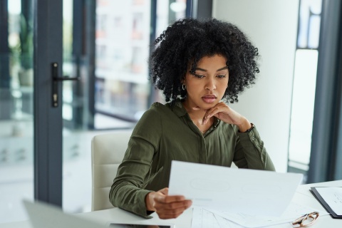 Woman reviewing paperwork at a desk in bright indoor setting.
