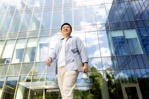 Businessman walking outside of an office building in Malaysia holding a laptop