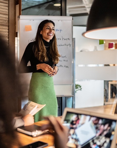 Woman hosting a working session at the front of a meeting room.