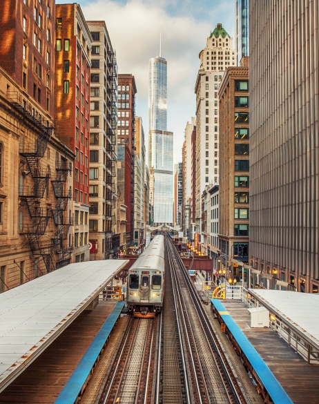Chicago railway between high rises with metro approaching and cityscape in the background.