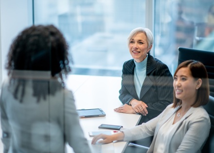 Three female HR professionals discuss work-related matters while gathered around an office conference room table