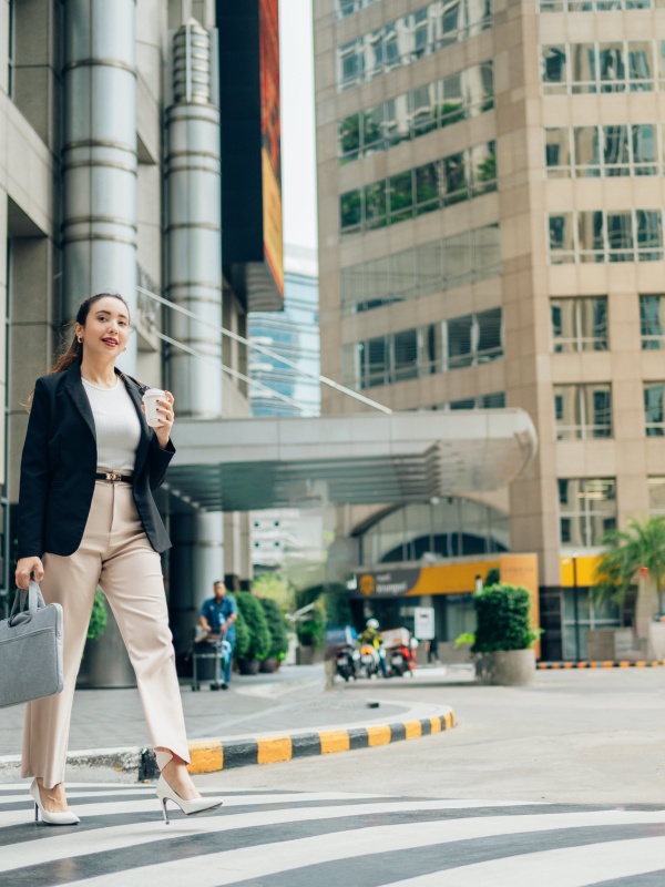 Woman crossing the street with a coffee, while considering EOR services in the Philippines.