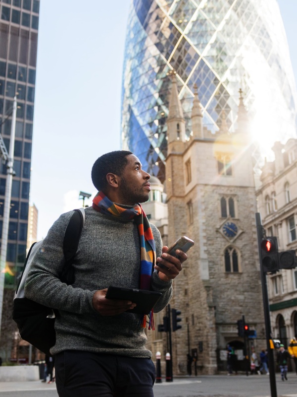Man holding a mobile phone, crossing the street while considering EOR services in the U.K.
