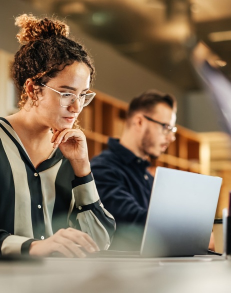 Colleagues sitting side-by-side on desk working on individual laptops.