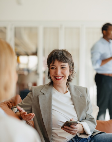Woman in business casual attire holding phone and discussing M&A with colleagues.