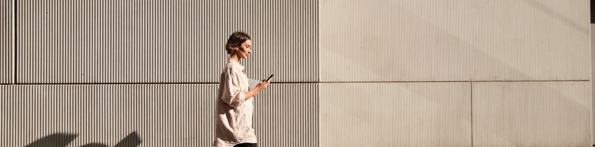 Confident businesswoman walking on street while looking at phone during sunset.