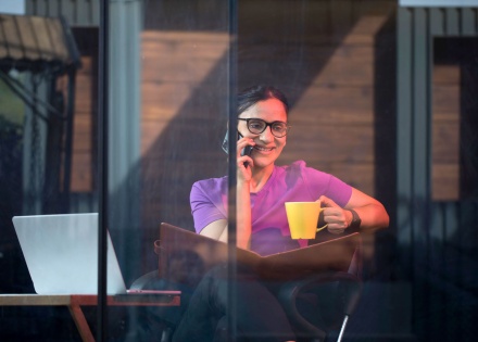 A remote employee in India engages in a work call on her mobile phone while working in a public coffee shop