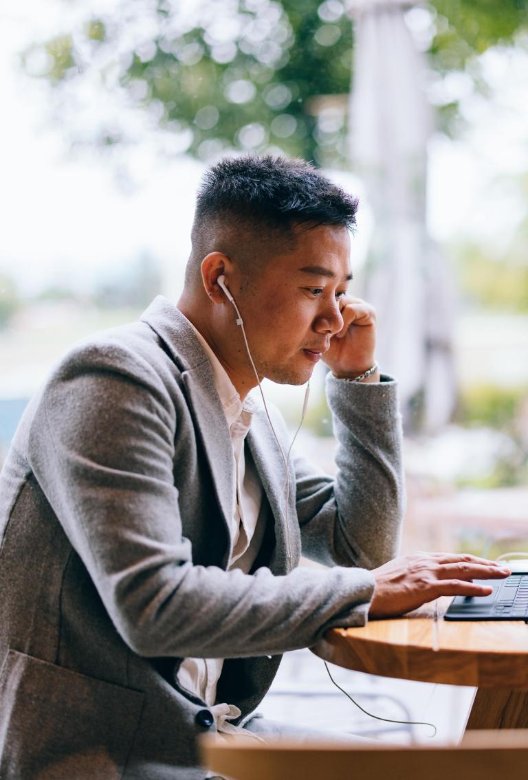 Professional legal team employee reviewing Pebl EOR services on laptop outdoors with headphones in and coffee.
