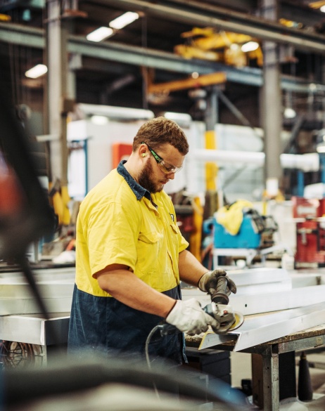 Man working with tool in manufacturing plant wearing gloves and safety glasses.