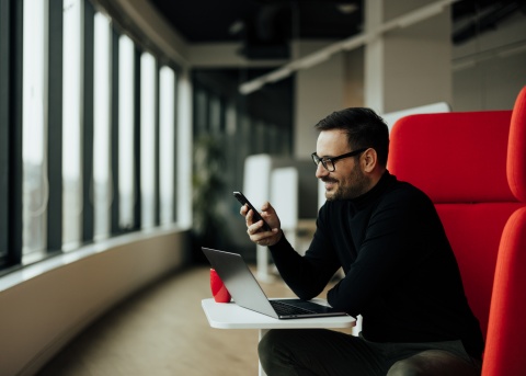 Male business leader managing work operations from his smartphone and laptop