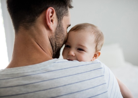 A new father lovingly holding his baby son while on paternity leave