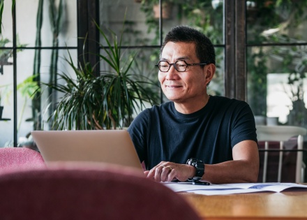 Man sitting at desk smiling while working on a laptop
