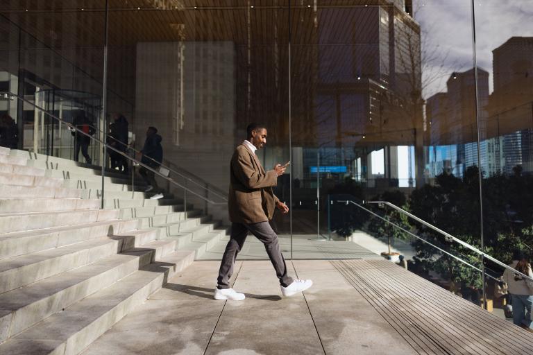 Professional businessman looking at phone while walking down stairs outdoors.