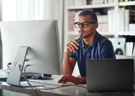 Man working remotely, looking at computer screen with bookshelf background