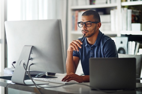 Man working remotely, looking at computer screen with bookshelf background