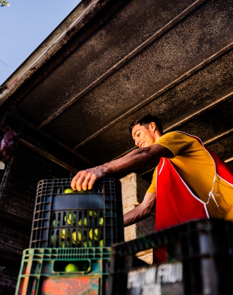 Young man unloading fruit from large truck.