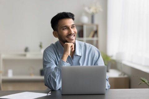 Smiling man sitting at a desk with his laptop in Malaysia
