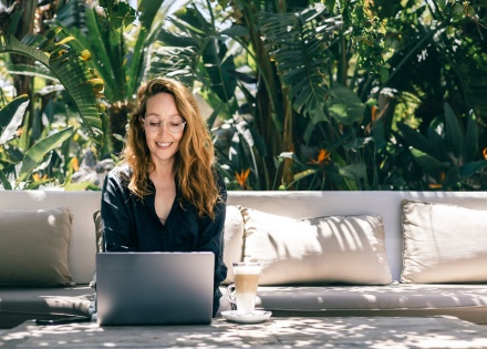 Smiling woman working on laptop outdoors in tropical garden
