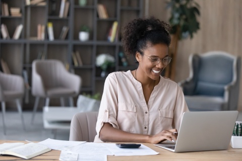 Smiling young woman reading about payroll taxes in Jamaica on her laptop