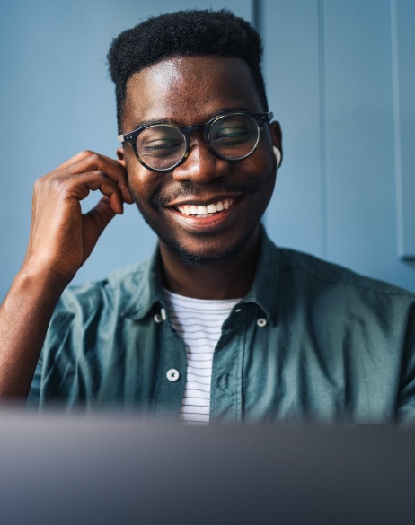 Male employer smiling and adjusting airpods while looking at computer with blue background.
