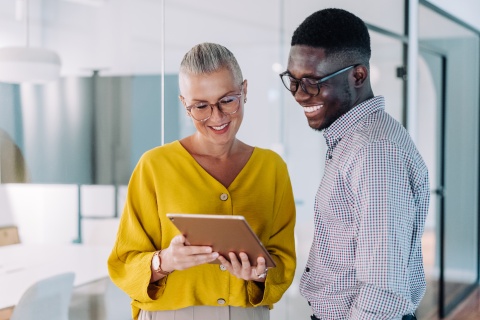 Two colleagues using a digital tablet and discussing payroll tax in Estonia
