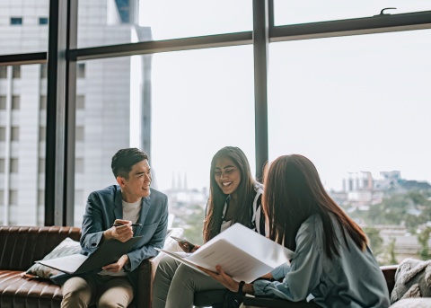 Three people sitting along a window and chatting