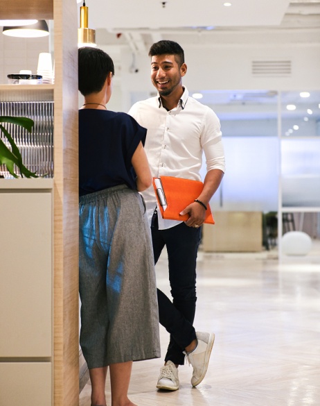 Two H1B visa employees at an AI company smiling and chatting while holding a laptop