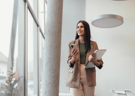 Young businesswoman walking in modern office holidaying a laptop and smartphone