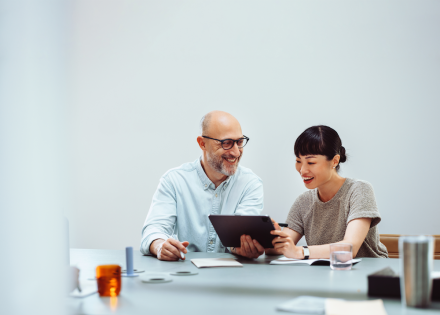 Two coworkers sitting at a table looking at a tablet.